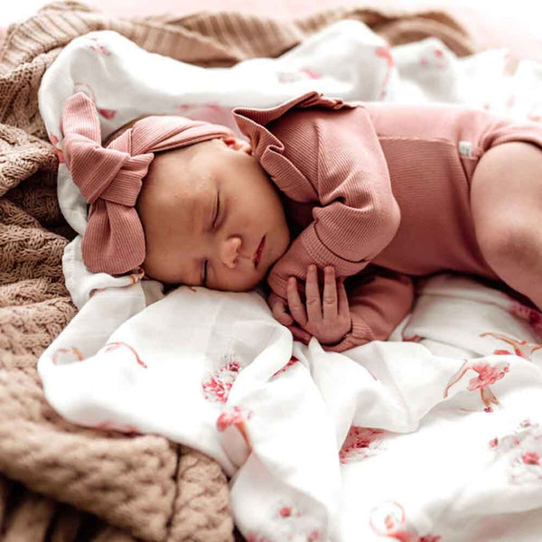 Newborn baby in pink outfit and headband lying on floral blanket