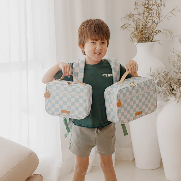 Child holding two checkered bags in a bright room with plants