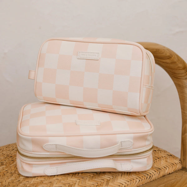 Two pink checkered toiletry bags stacked on a woven surface.
