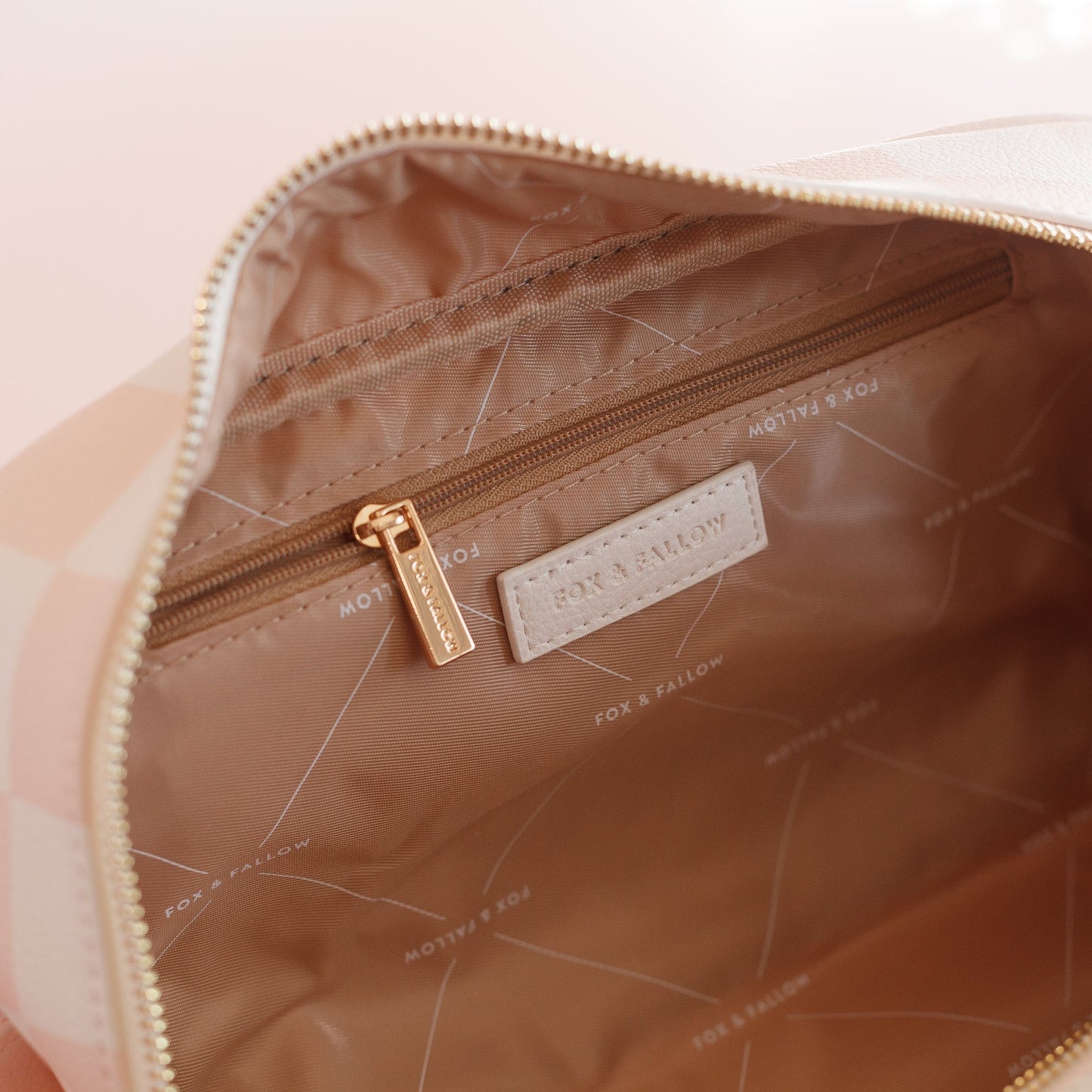 Close-up of a checkered washbag with a visible brand label on a light pink background