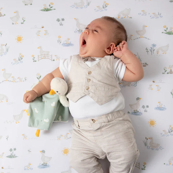 Baby in formal attire lying on a patterned surface with a toy duck
