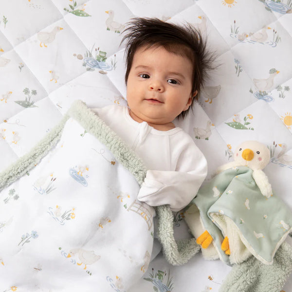 Baby lying on a quilted blanket with a soft toy, surrounded by a cozy and patterned background.