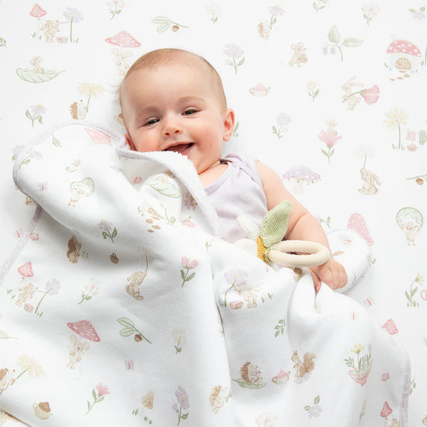 Baby wrapped in a floral-patterned blanket with a toy, on a white background