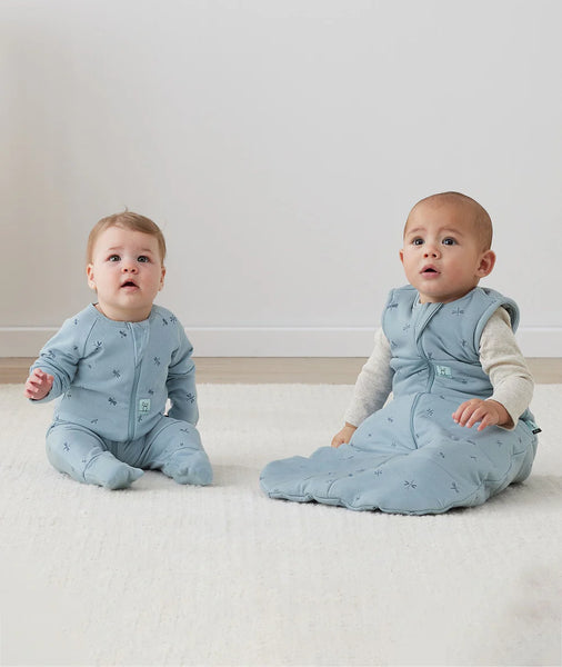 Two babies wearing matching blue outfits sitting on a light-colored floor.