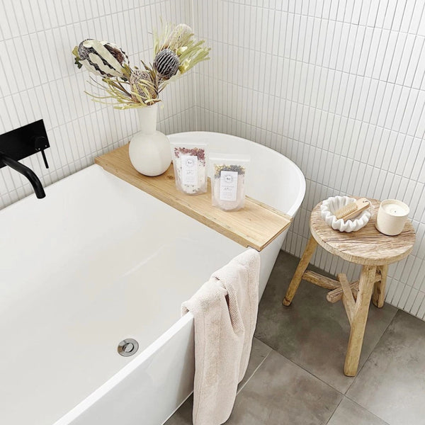 Bathroom with a bathtub, wooden tray, and small stool.