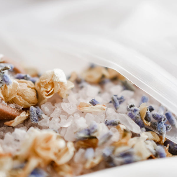 Close-up of a bath salt mixture with flowers and lavender petals in a white container.