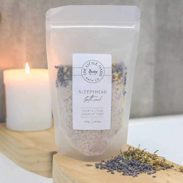Bag of bath salts with lavender and eucalyptus next to a lit candle on a wooden surface.