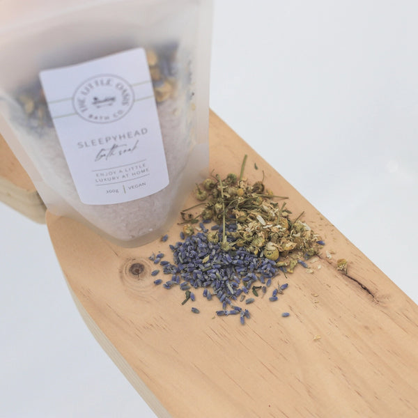 Bath salt packaging labeled 'Sleepyhead' with lavender buds on a wooden board.