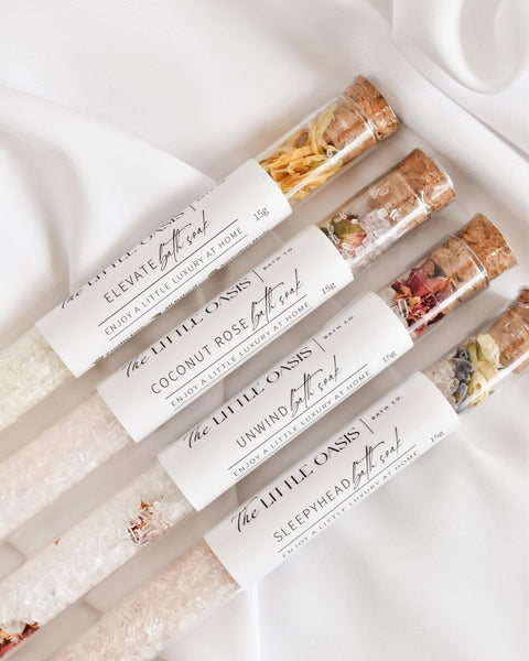 Row of bath salts in clear containers with visible labels on a white background