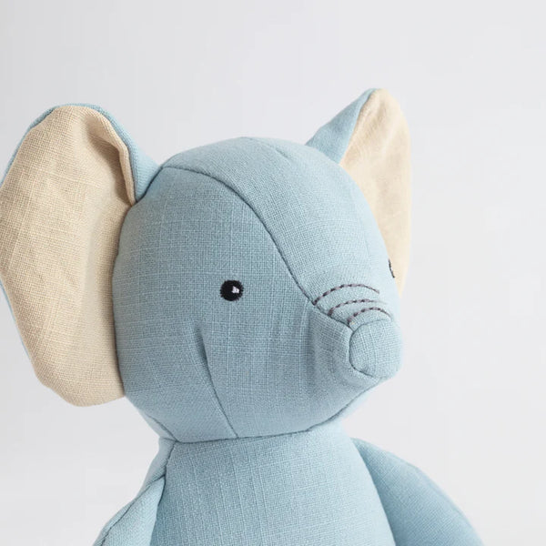 Close-up of a soft toy elephant with beige ears on a light gray background
