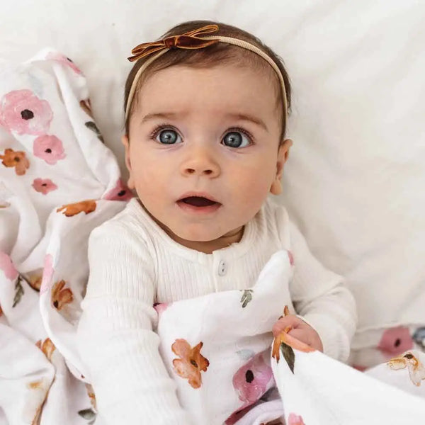 Baby with wide eyes and a headband, surrounded by floral blankets