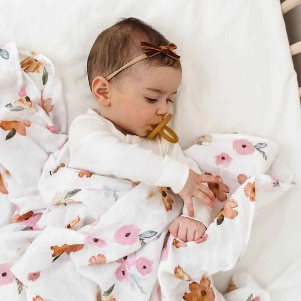 Baby wrapped in a floral blanket with a pacifier, lying on a white surface.