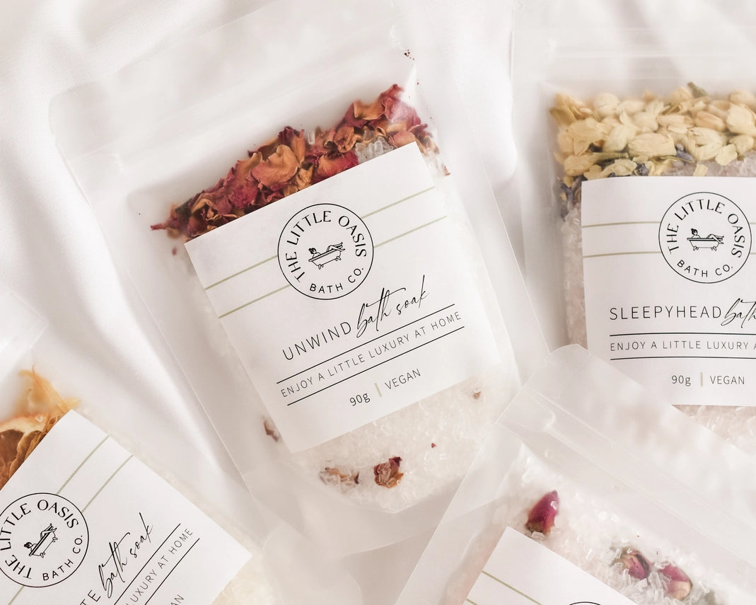 Bath soaks with decorative elements and 'The Little Oasis Bath Co.' branding on a soft white background.