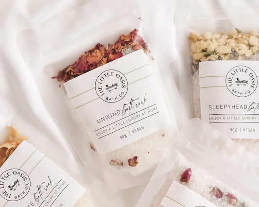 Bath soaks with decorative elements and 'The Little Oasis Bath Co.' branding on a soft white background.