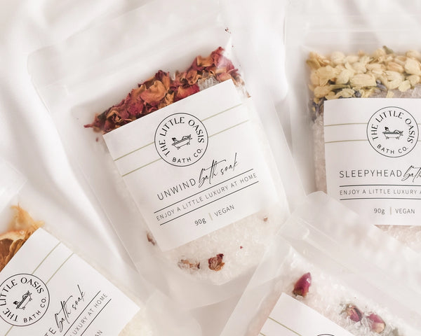 Bath soaks with decorative elements and 'The Little Oasis Bath Co.' branding on a soft white background.