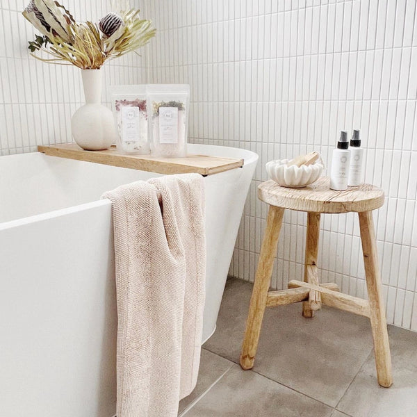 Bathroom setting with a freestanding bathtub, wooden stool, and decorative items.