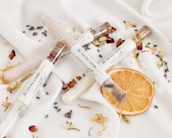 Three small glass jars with dried herbs and flowers on a white surface with an orange slice.