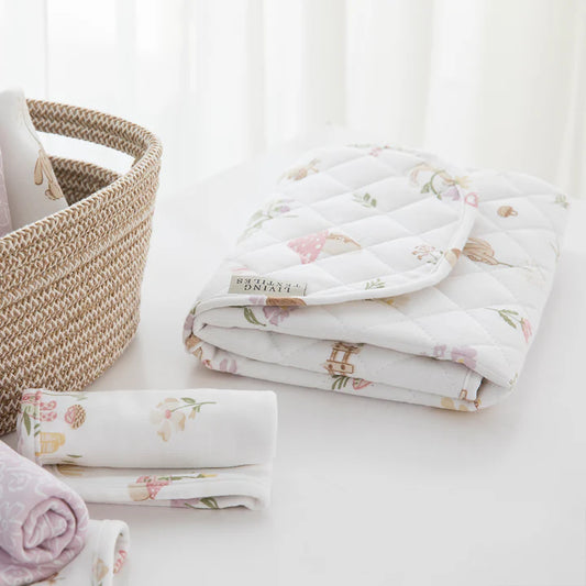 Floral-patterned baby blankets stacked on a white surface with a woven basket.
