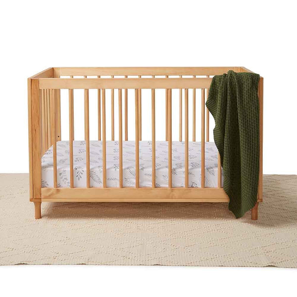 Wooden crib with a green blanket and white mattress on a beige surface.