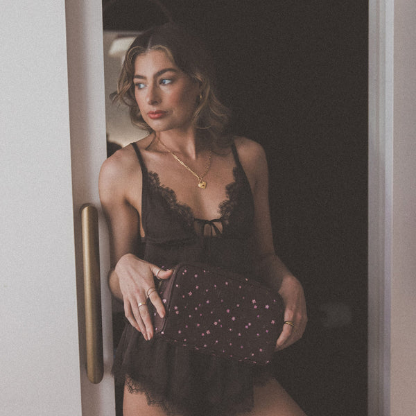 Woman in black lace lingerie holding a clutch in a dimly lit room.