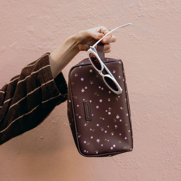 Hand holding a patterned bag with sunglasses on a pink background
