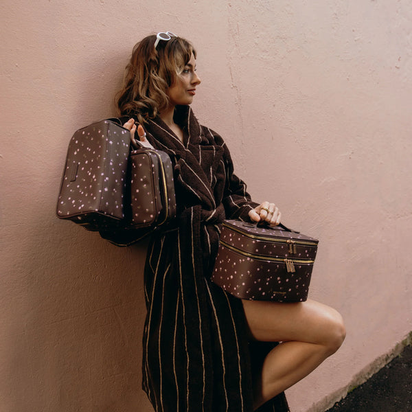 Woman in a robe holding patterned bags against a pink wall