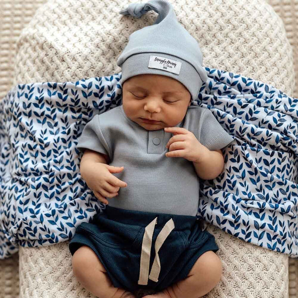 Newborn baby in gray outfit and hat lying on a patterned blanket