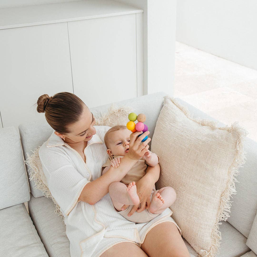Woman holding a baby on a couch with a colorful toy