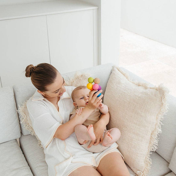 Woman holding a baby on a couch with a colorful toy
