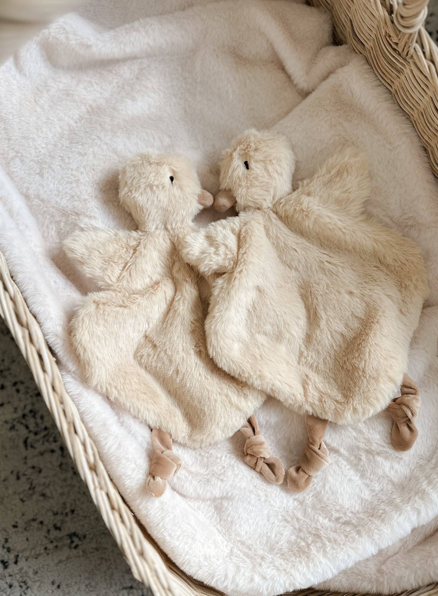 Two fluffy white duck toys on a textured blanket