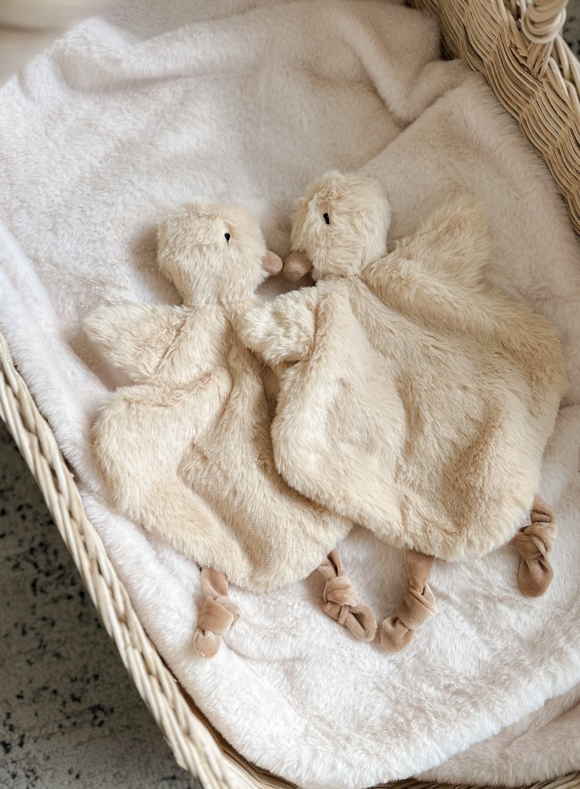 Two fluffy white duck toys on a textured blanket