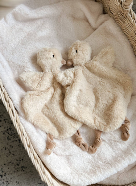 Two fluffy white duck toys on a textured blanket
