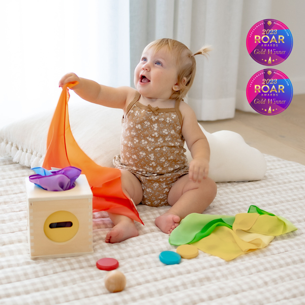 Baby playing with colorful toys on a bed, with ROAR awards visible