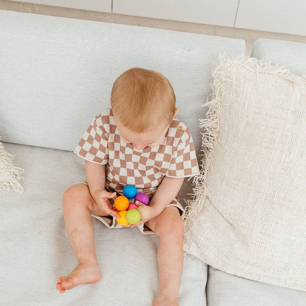 Baby sitting on a couch holding colorful balls