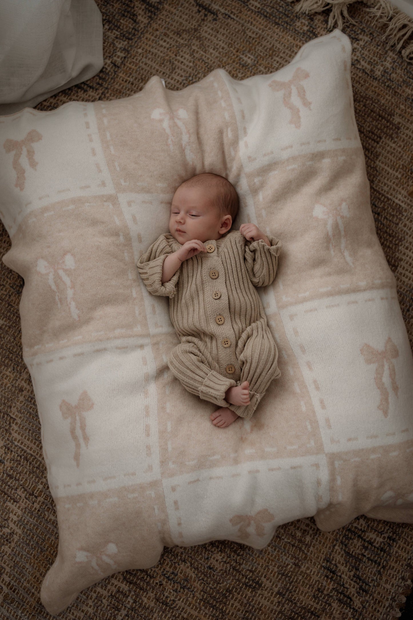 Newborn baby in a beige outfit lying on a textured pillow with a natural background