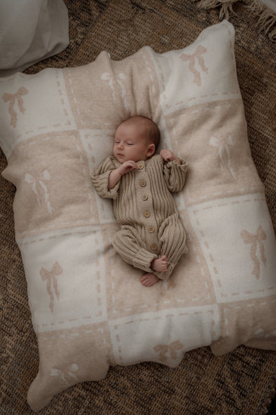 Newborn baby in a beige outfit lying on a textured pillow with a natural background