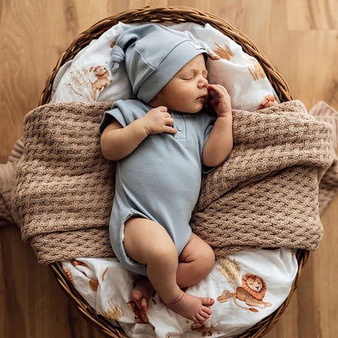 baby lying in a bassinet in a snuggle hunny bodysuit and on a blanket